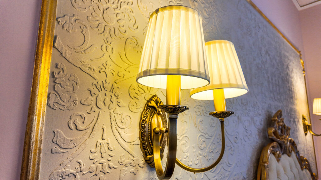 Applique dorata con due paralumi plissettati su una parete decorata